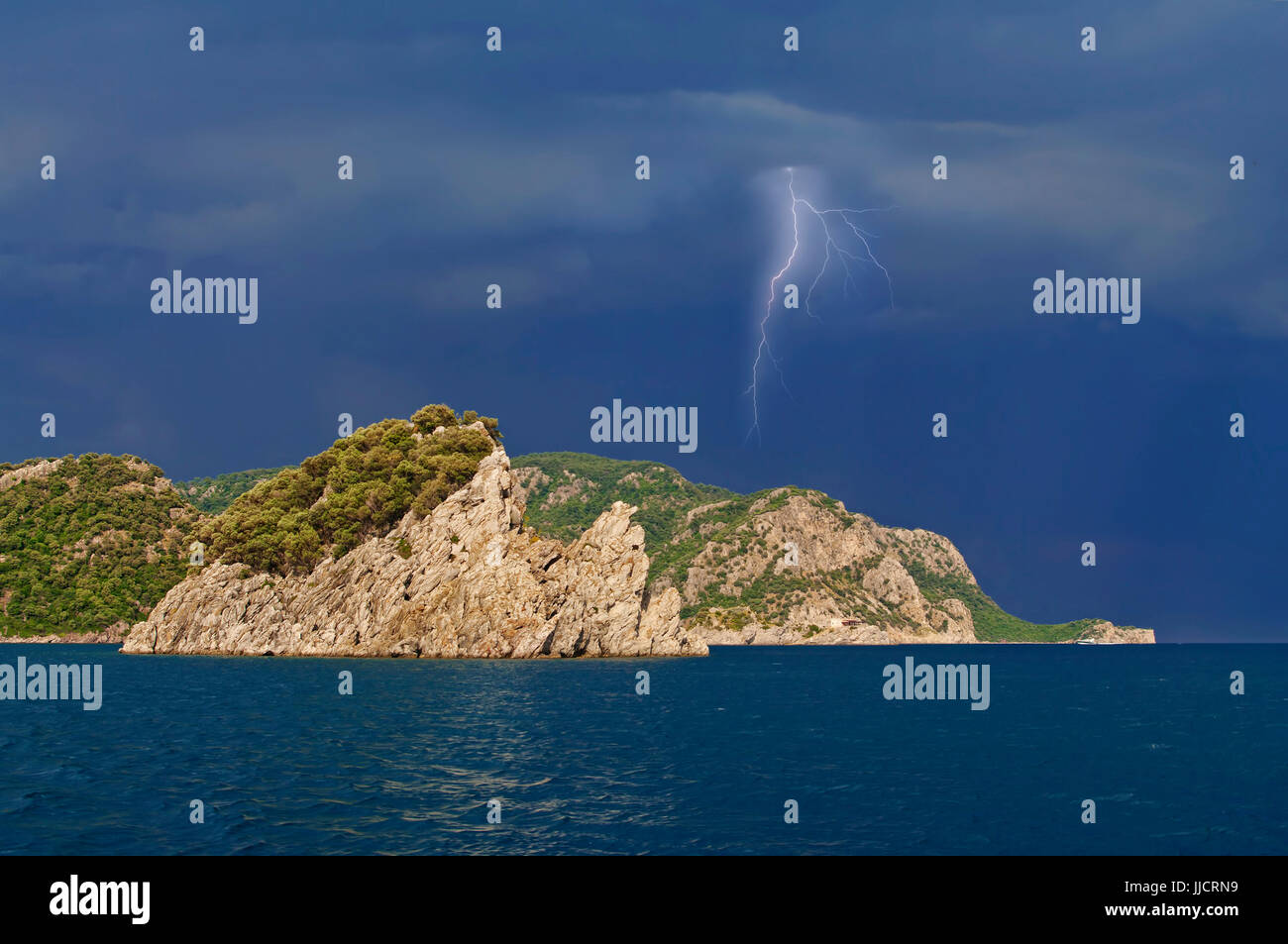 lightning striking over sunlit rocky island during thunderstorm in Aegean sea near Marmaris, Turkey Stock Photo