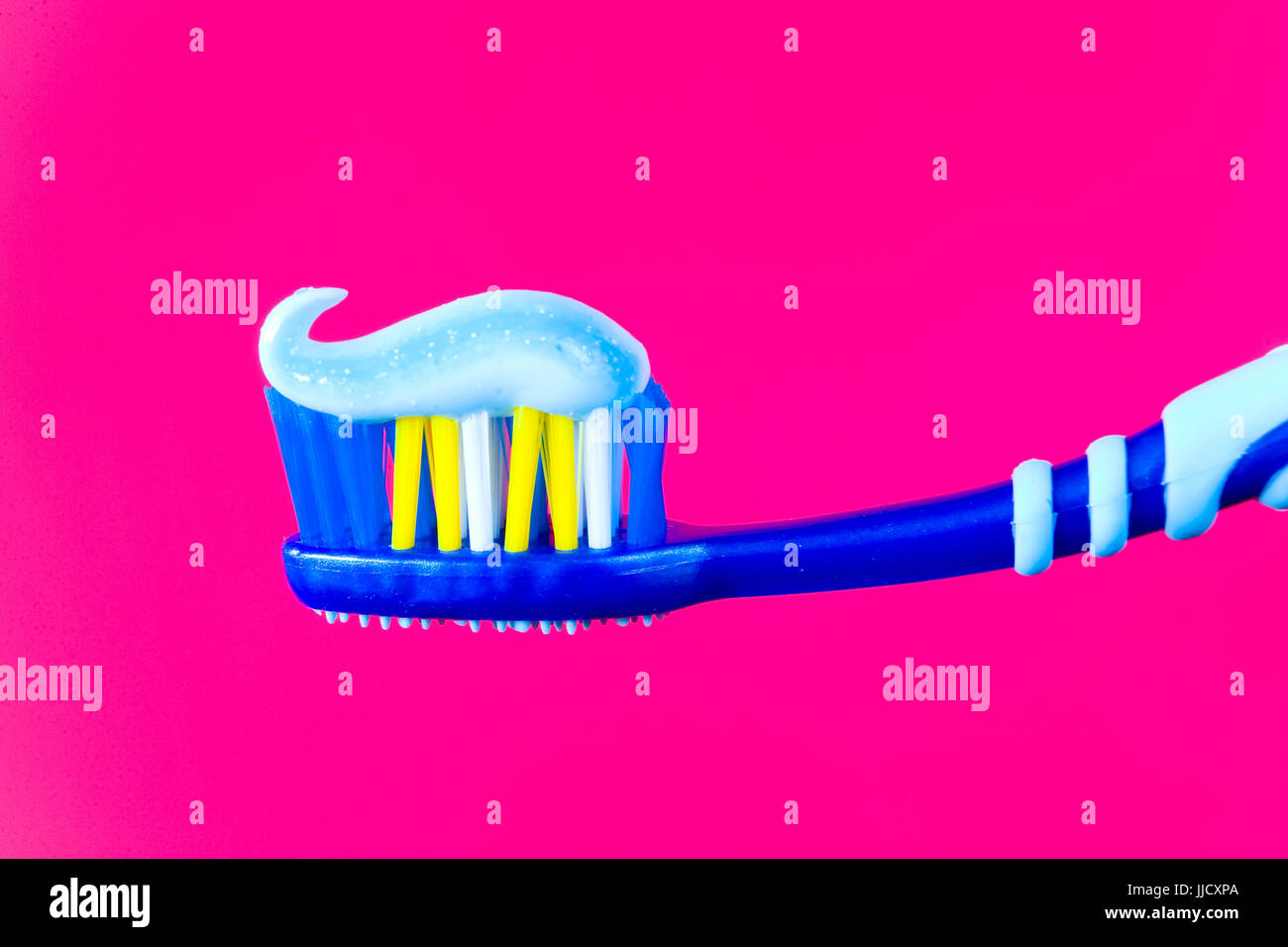 Means of personal hygiene. Blue toothbrush with blue toothpaste on a crimson background. Stock Photo