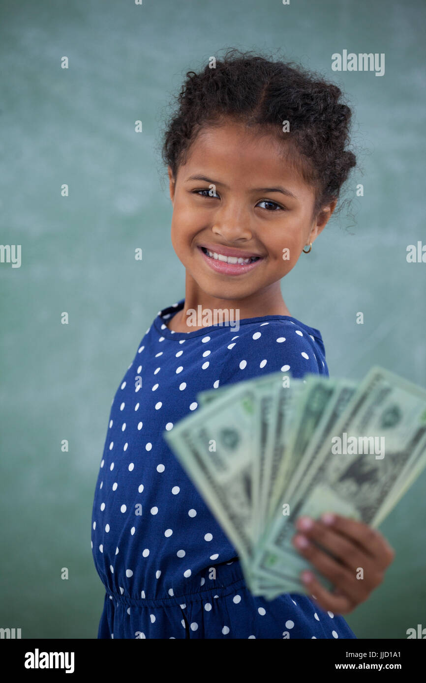 Portrait of girl showing paper currency while standing against wall Stock Photo