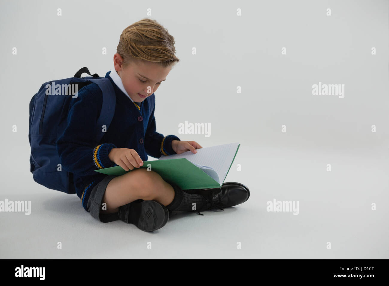 Adorable schoolboy reading book while sitting on white background Stock ...