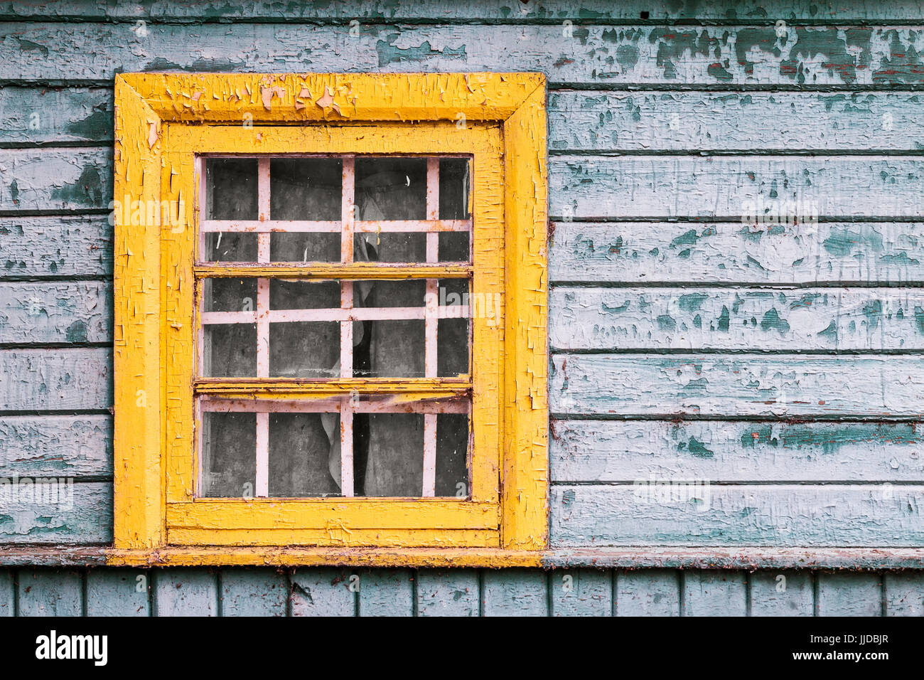 small yellow window on green wooden wall of abandoned house Stock Photo