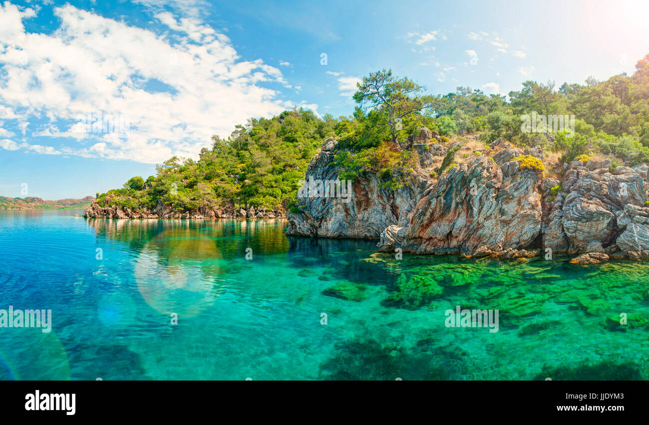 panoramic view of turquoise blue lagoon in Aegean Sea surrounded by rocks and trees brightly lit with sinlight, Turkey Stock Photo