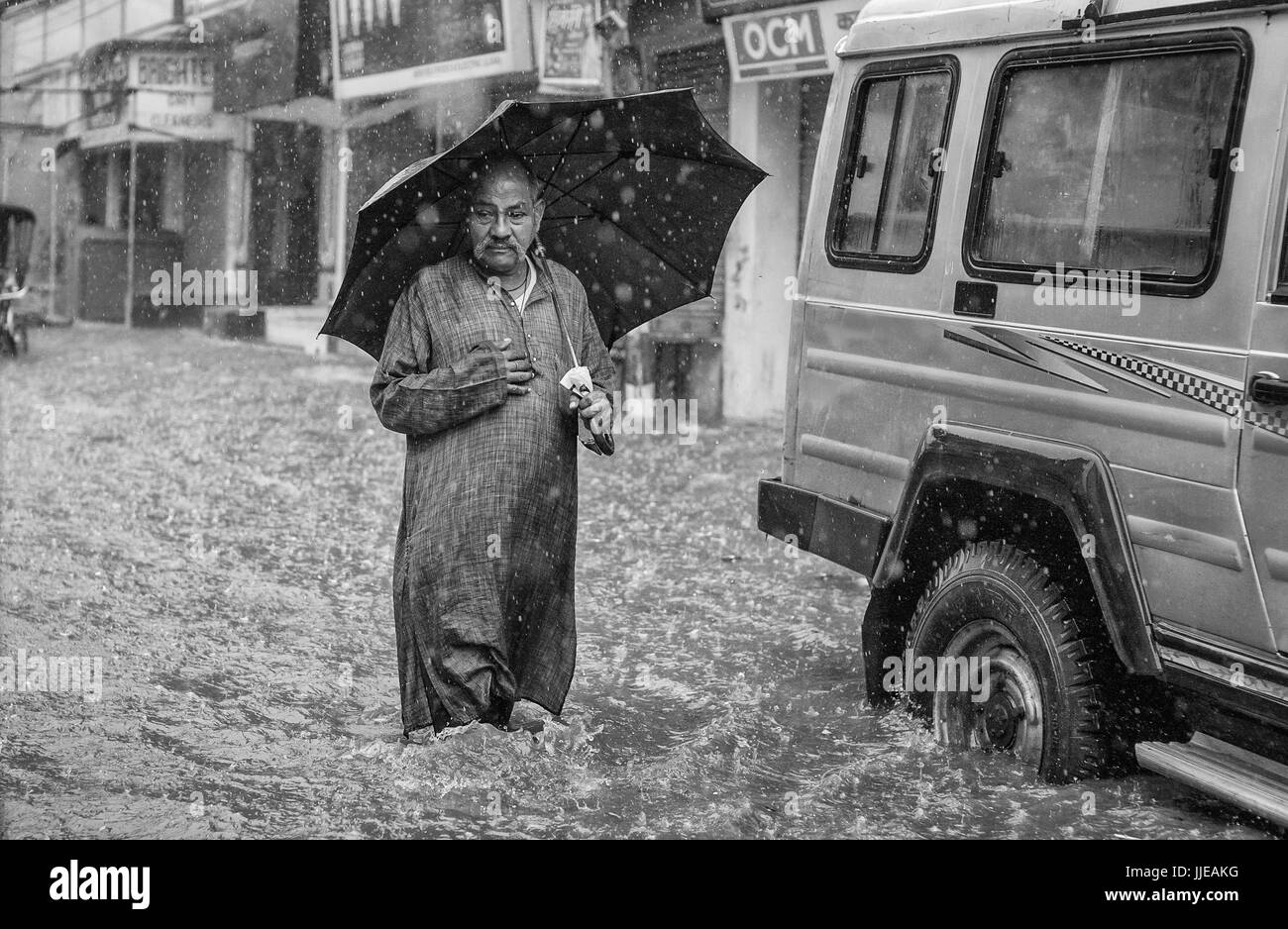 Man is distress with his knees deep in monsoon floods and rain walking along street in Varanasi, Uttar Pradesh, India. Stock Photo