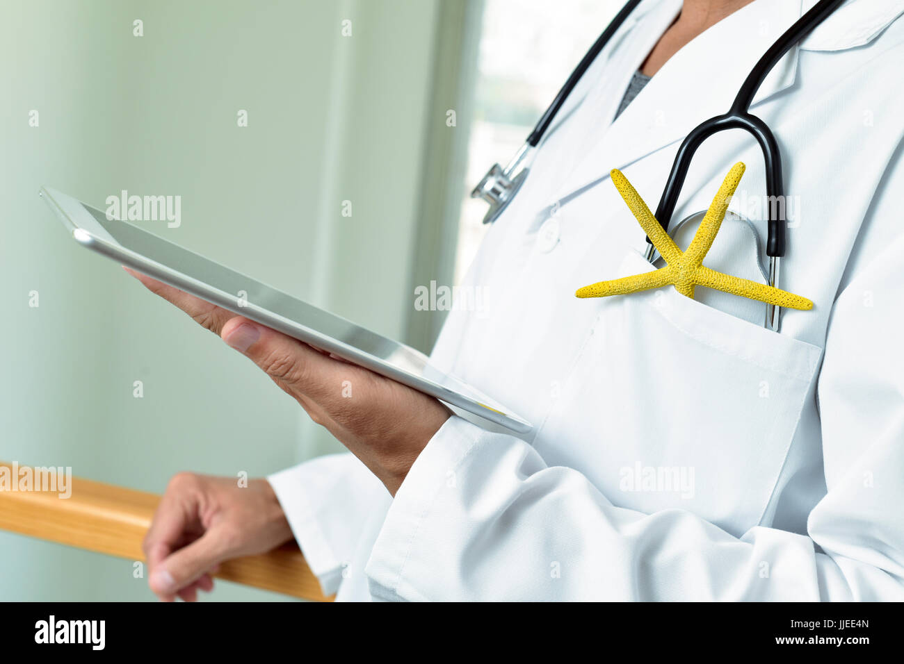 closeup of a young caucasian doctor man using a tablet with a colorful yellow starfish and a stethoscope in the pocket of his white coat, depicting th Stock Photo
