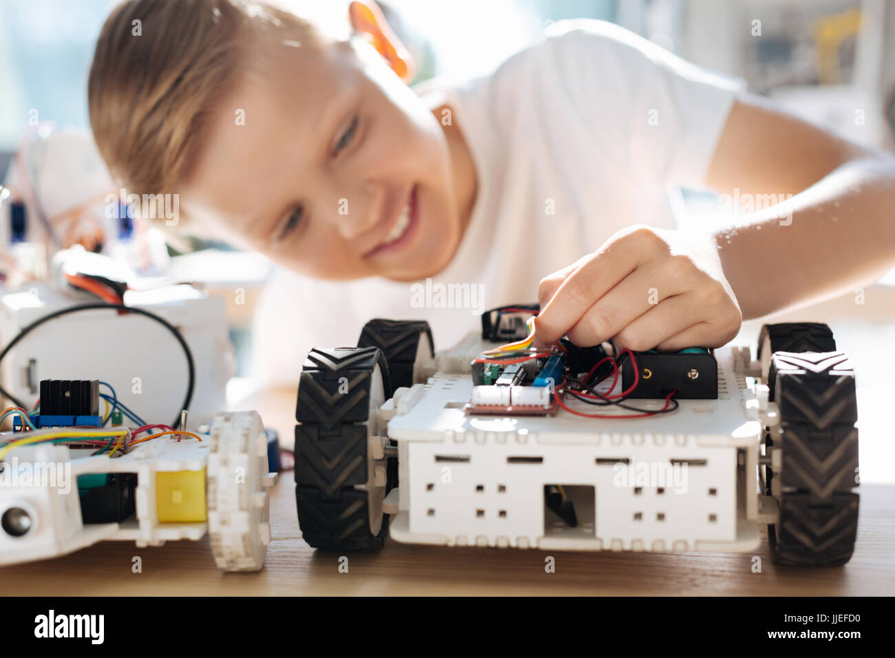 Fair-haired boy adjusting wires in robotic car Stock Photo