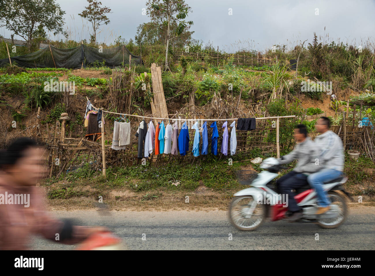 Shirts hang to dry alongside roadside gardens in Phongsaly, Laos as scooters speed past. Stock Photo
