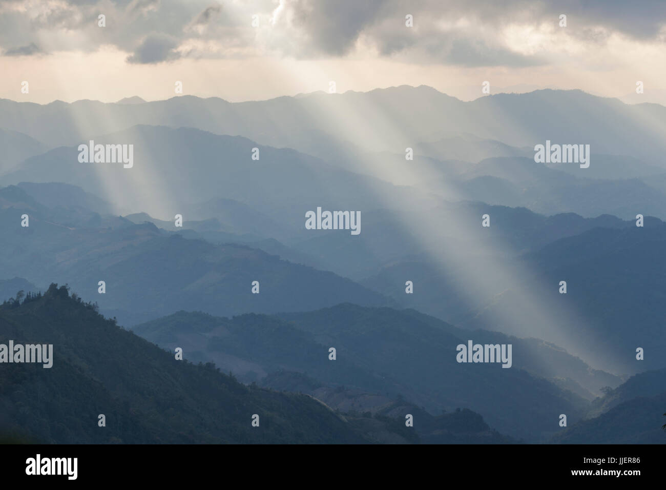 Shafts of sunlight illuminate the hills surrounding Phongsaly, Laos from the summit of Phoufa (1626 m). Stock Photo
