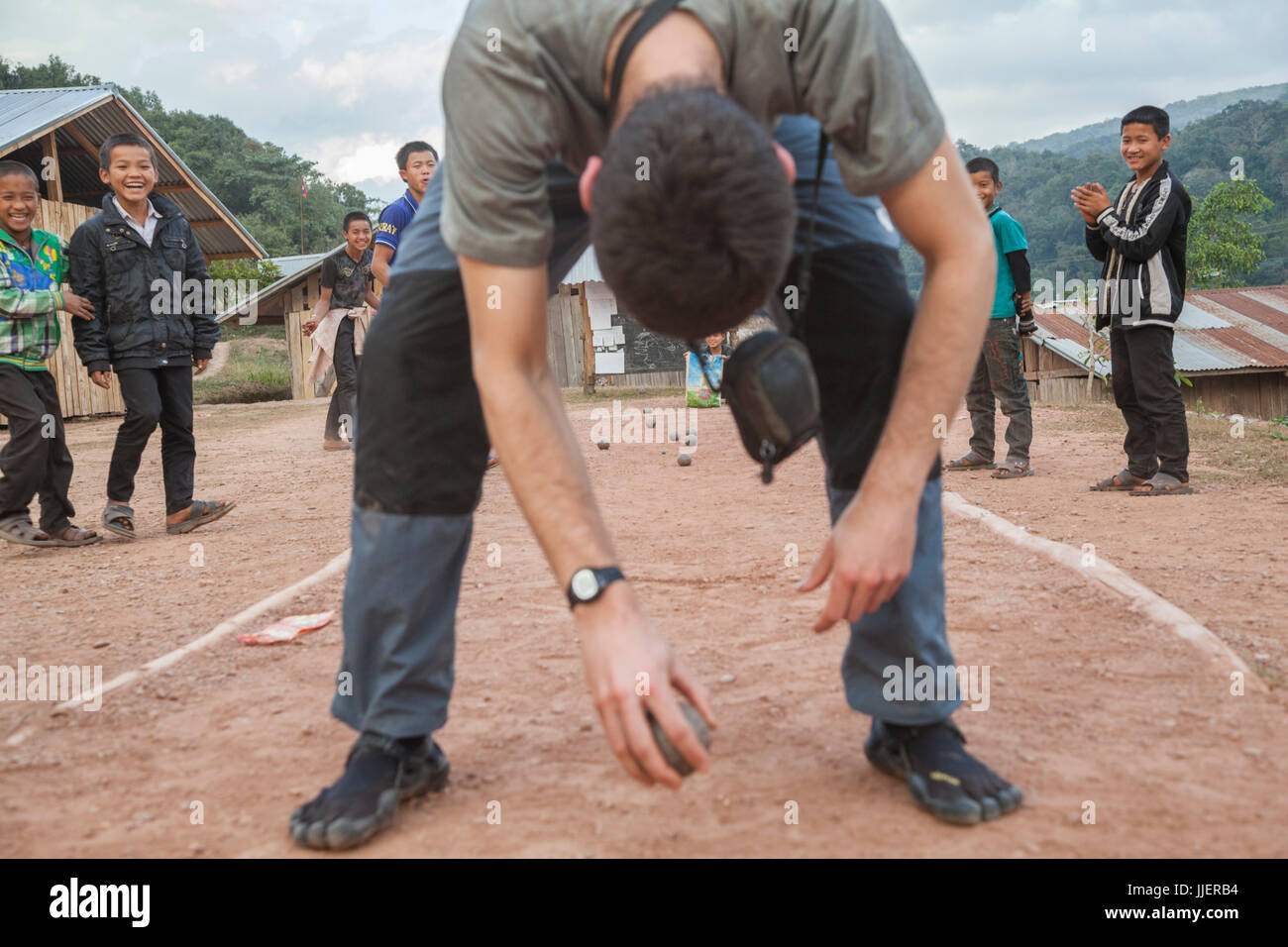 Robert Hahn plays boules (pétanque) with students at a boarding school, jokingly throwing the ball between his legs, in Ban Tang, Laos. Stock Photo