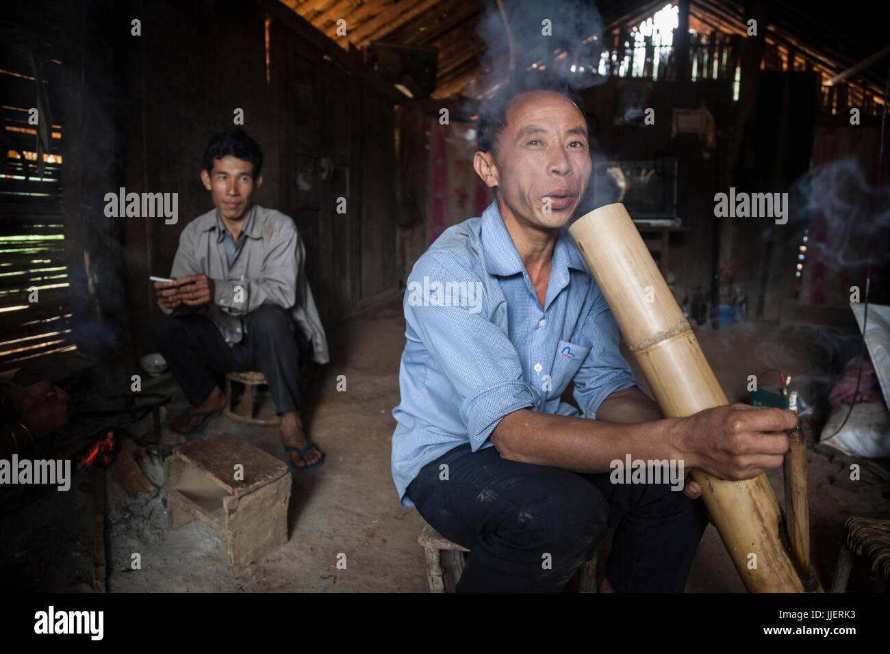 A man smokes a cigarette through a large bamboo water bong at his home in Ban Sop Kha, Laos. He explained that smoking cigarettes this way was better for his lungs. Stock Photo