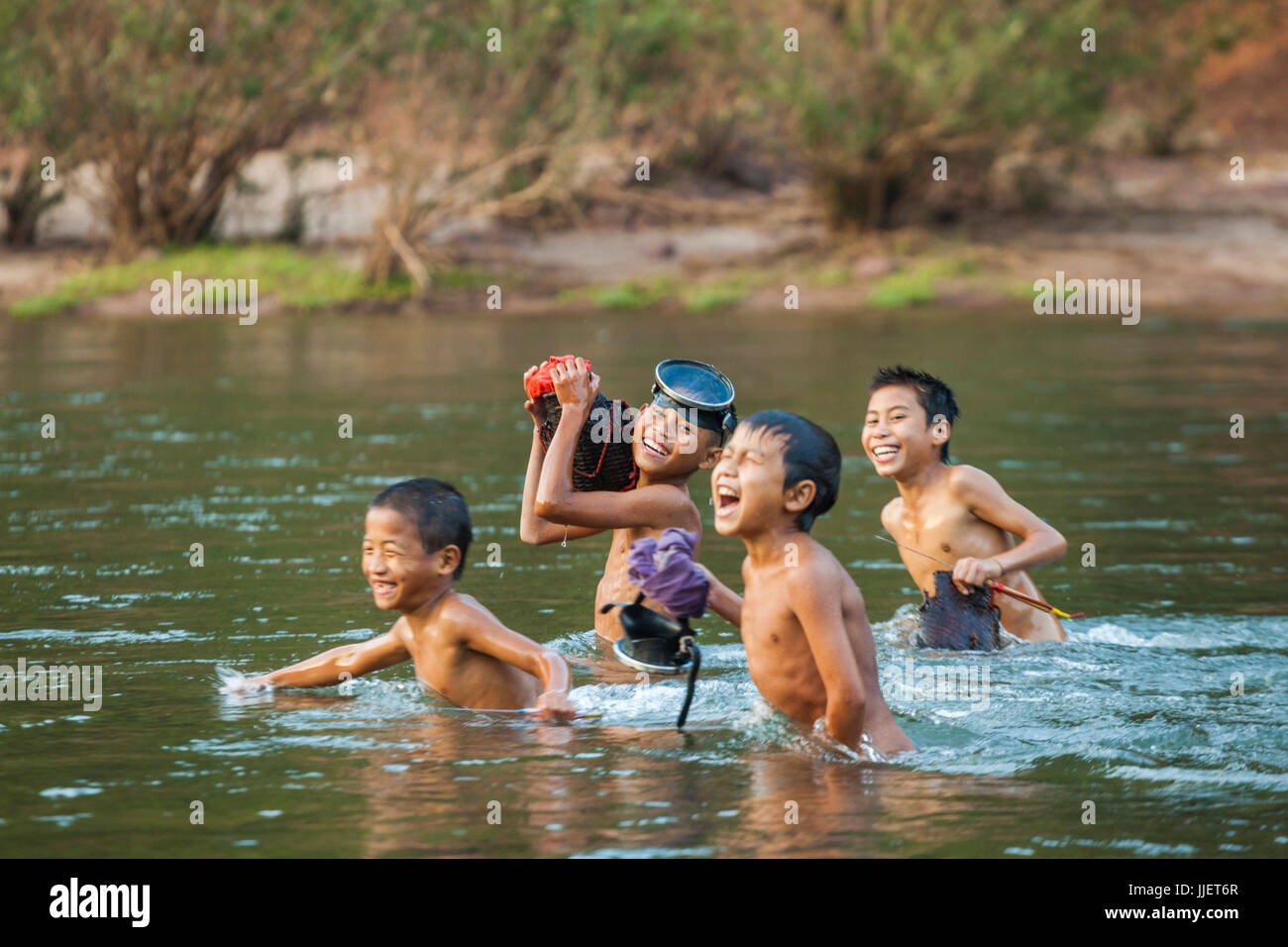 Naked young boys emerge from the water returning from spear fishing in the Nam Ou River outside Muang Hat Hin, Laos. Stock Photo