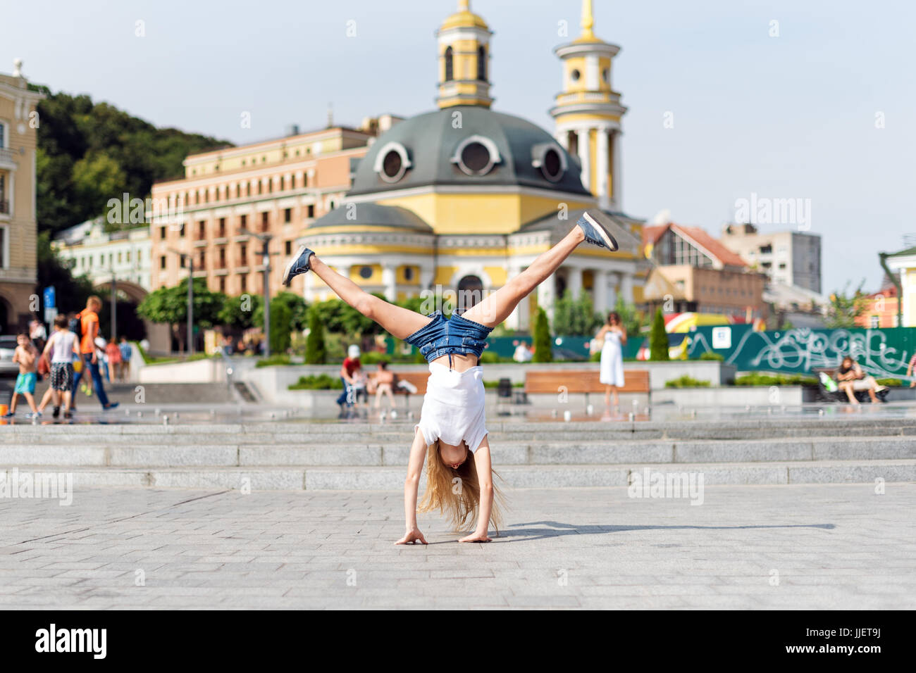 Active kid girl gymnast stretching and doing splits on the street. Young girl acrobat. The girl is engaged in gymnastics. Stock Photo