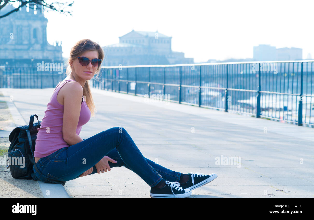 A girl in sunglasses sits on a curb in Dresden Stock Photo