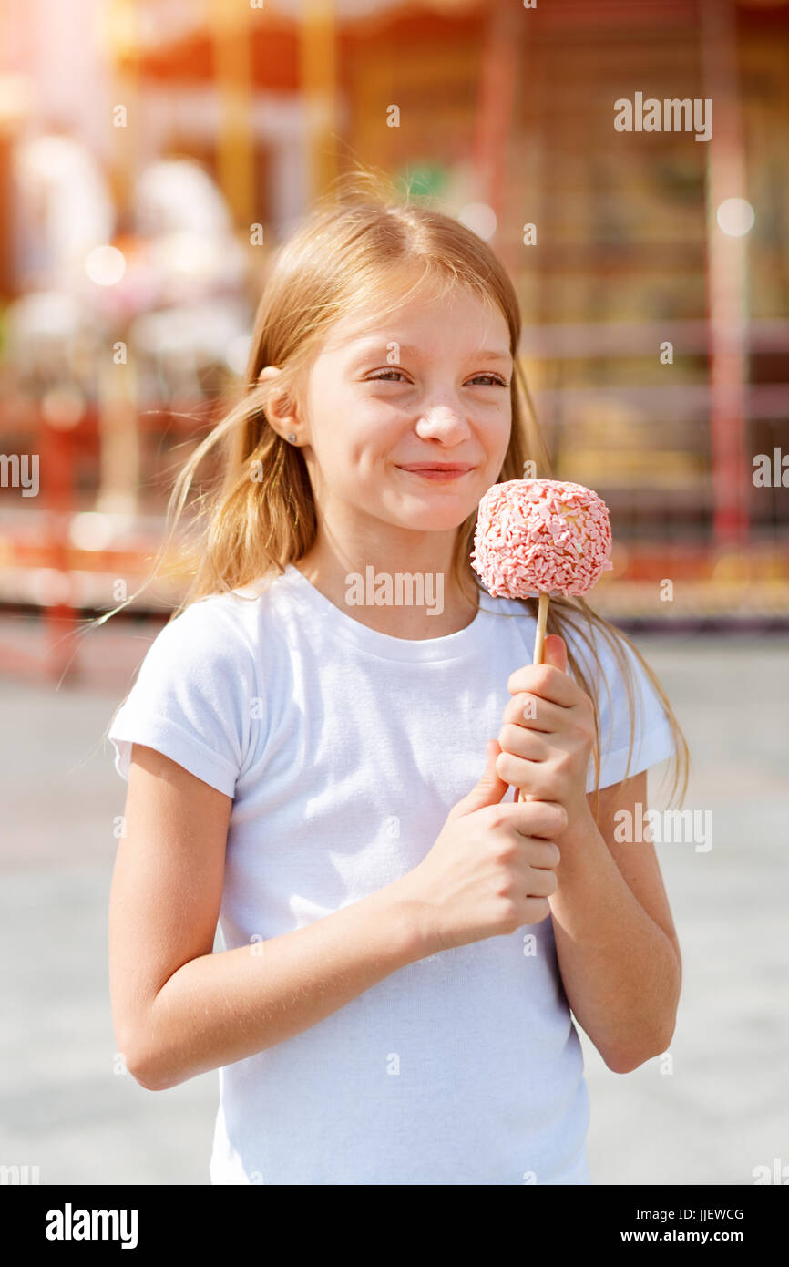 Cute little girl eating candy apple at fair in amusement park. Stock Photo