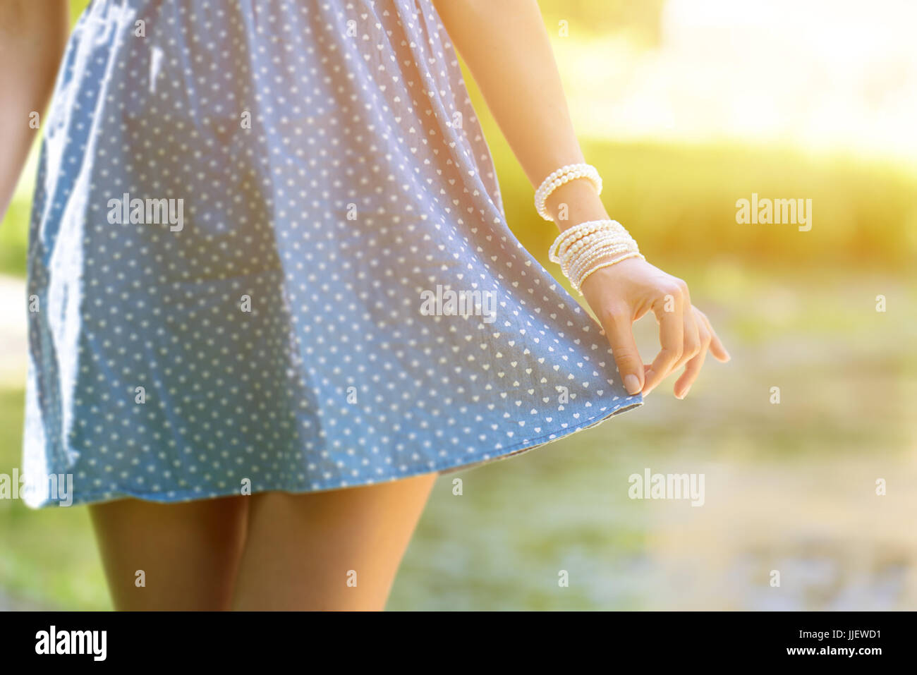 Beautiful young woman wear in a short dress. Girl holding hand edge of the skirt , close-up on green park background Stock Photo
