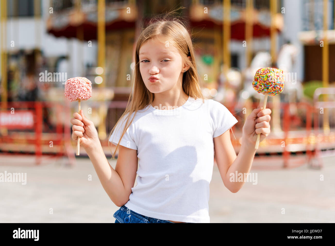 Cute little girl eating candy apple at fair in amusement park. Stock Photo