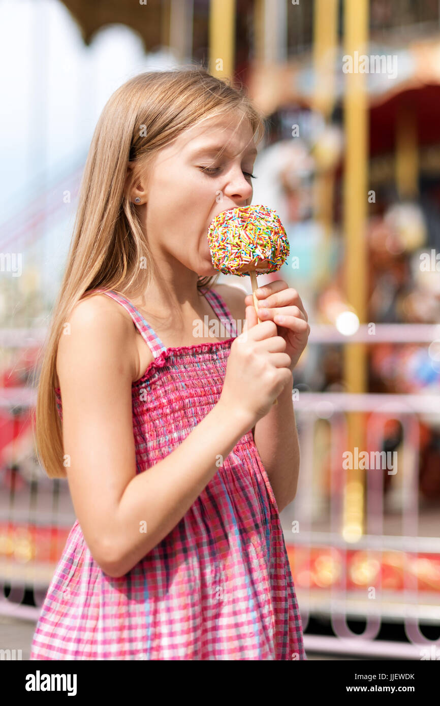 Cute little girl eating candy apple at fair in amusement park. Stock Photo