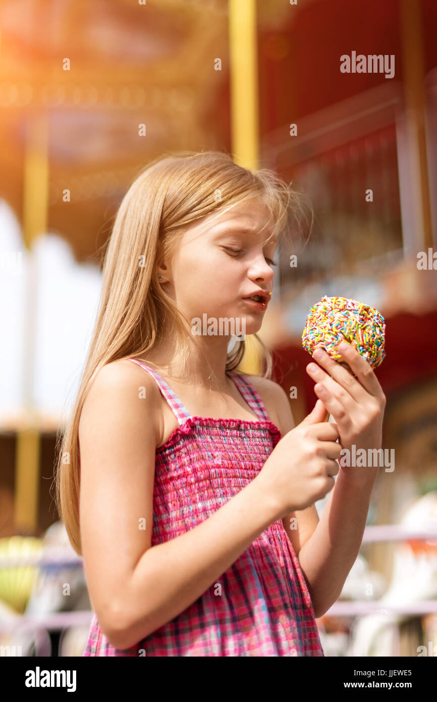 Cute little girl eating candy apple at fair in amusement park. Stock Photo