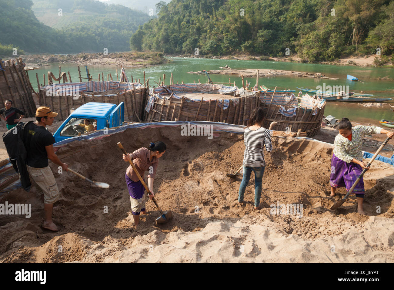 Loa men and women, working for SinoHydro, shovel sand on the shore of the Nam Ou River in Hat Sa, Laos. The sand is for making concrete used in the construction of Dam #6 being built upstream. Stock Photo