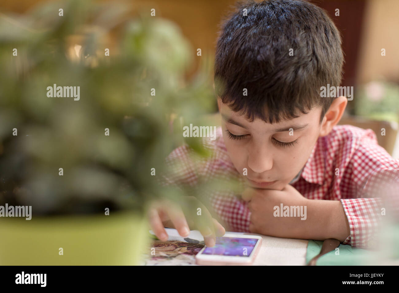 Boy sitting in a restaurant playing a game on his mobile phone Stock Photo