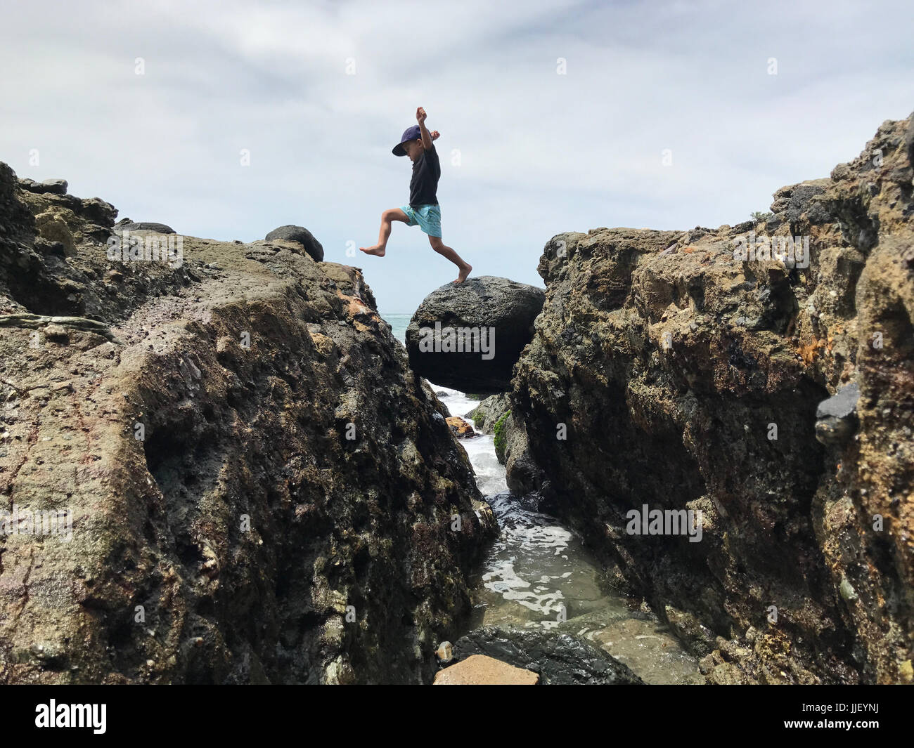 Boy jumping across rocks at the beach, California, America, USA Stock Photo