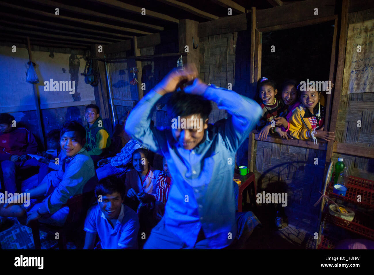 A young man shows off his moves at a party in Ban Huay Phouk, Laos as other partygoers, and young girls in the window, watch. The celebration was hoped to bring good luck to the woman of the house, who was suffering from cancer and whom modern western medicine had failed to treat. Stock Photo