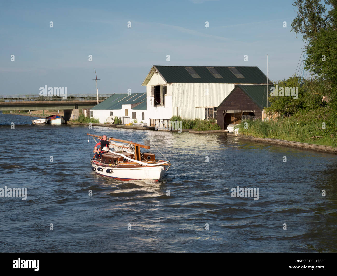 A yacht navigates the River Thurne at Potter Heigham on the Norfolk Broads UK in evening sunlight in summer Stock Photo