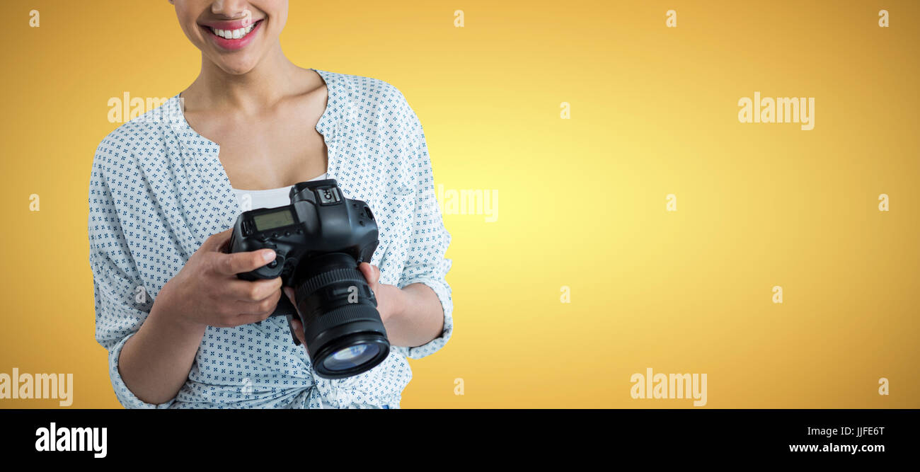 Portrait of smiling young woman holding digital camera against yellow ...