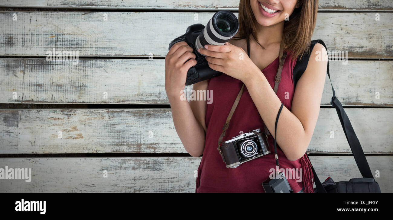 Portrait of smiling young woman holding digital camera against wood ...
