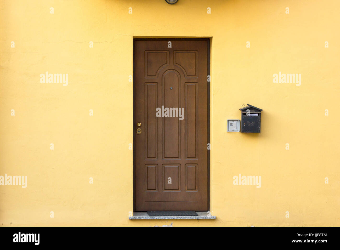 Single wooden entrance door of italian residential home building and yellow wall Stock Photo