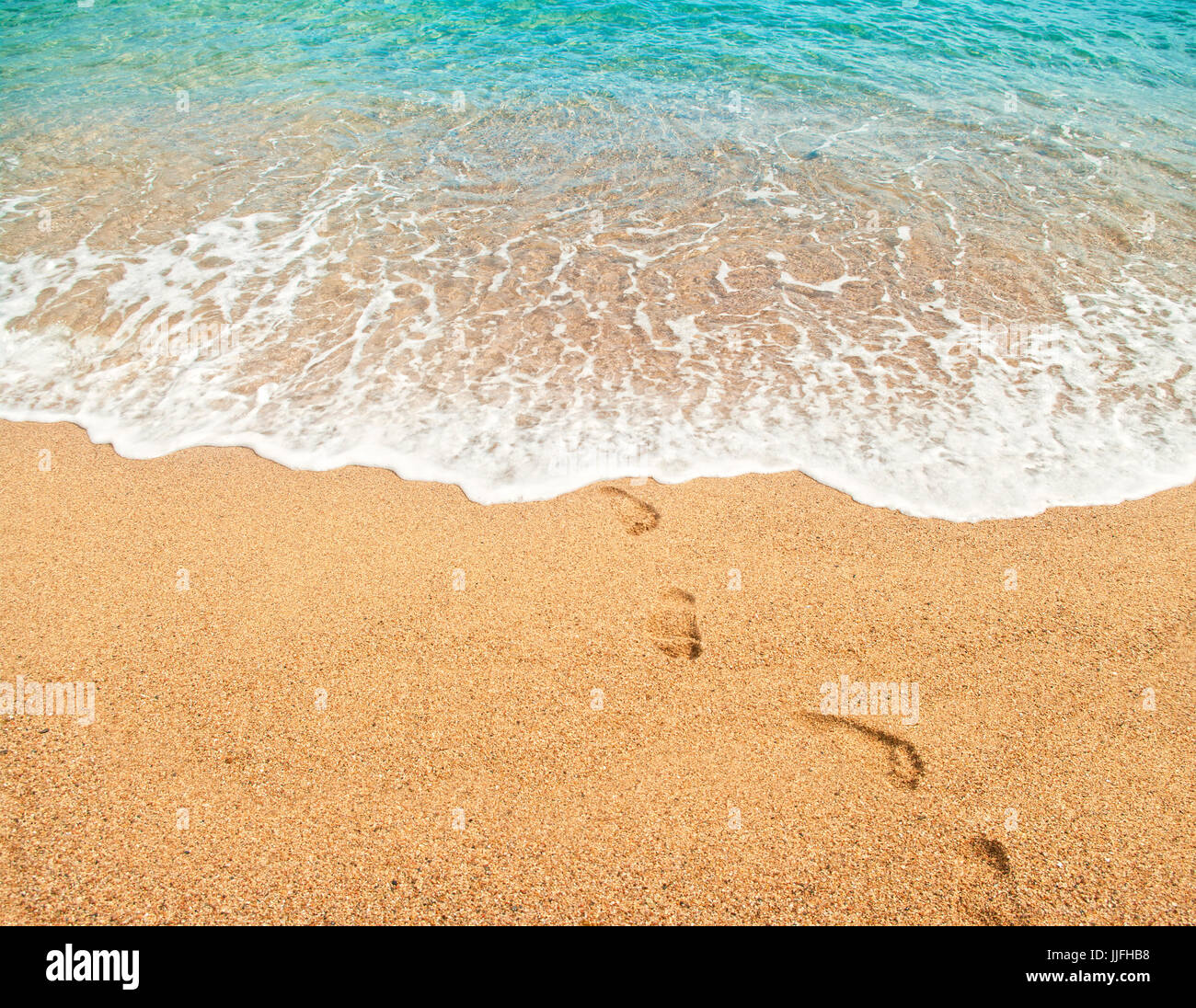 footprints on wet sand and beautiful turquoise water of mediterranean sea with soft white foam on sunny summer day in Spain Stock Photo
