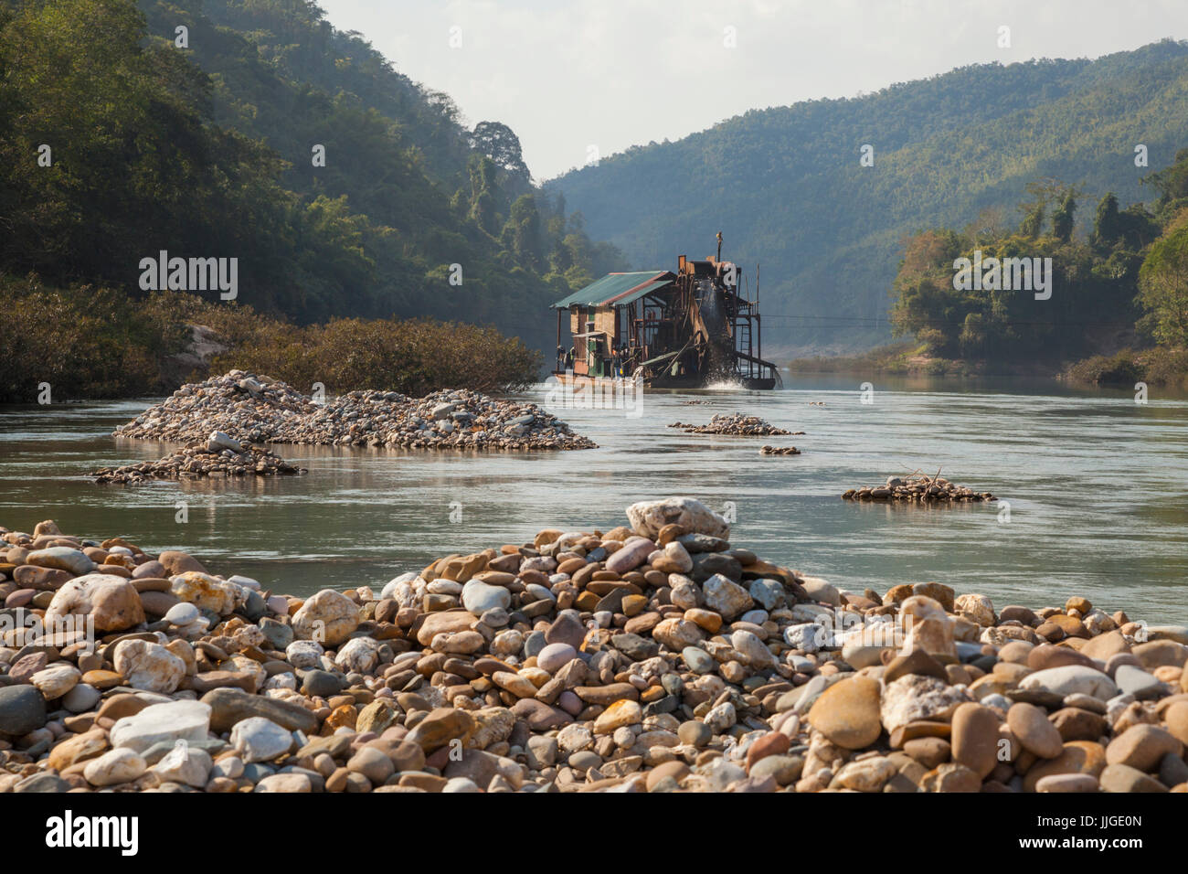 A floating Vietnamese mechanical gold dredge leaves a wake of tailing piles in the Nam Ou River, Laos. Stock Photo