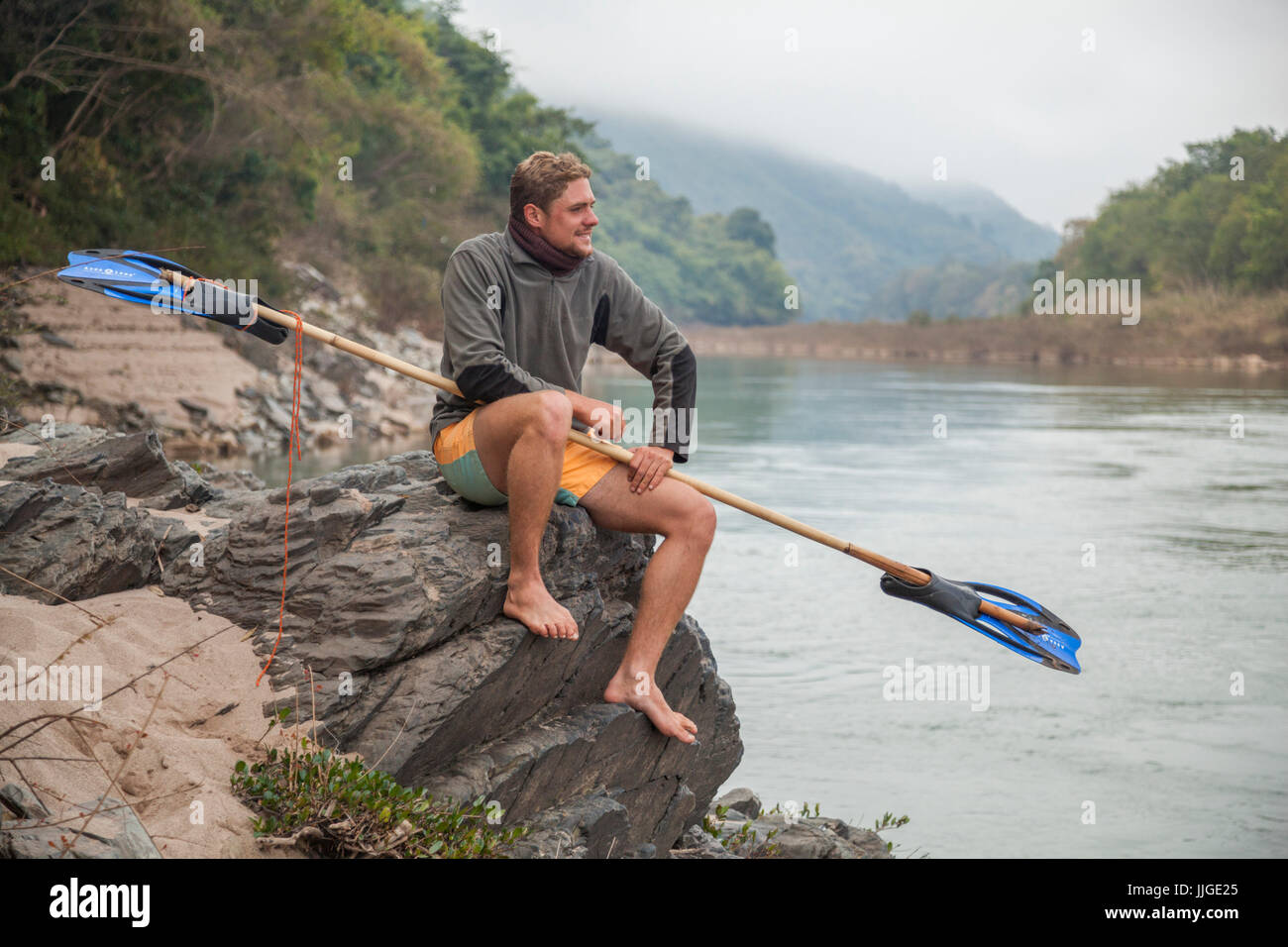Jan, from the Netherlands, poses with his bamboo and flipper paddle at this campsite on the shore of the Nam Ou River, Laos. He ultimately paddled from Muang Khua to Nong Khiaw on a bamboo raft he had constructed with the input of locals. Stock Photo