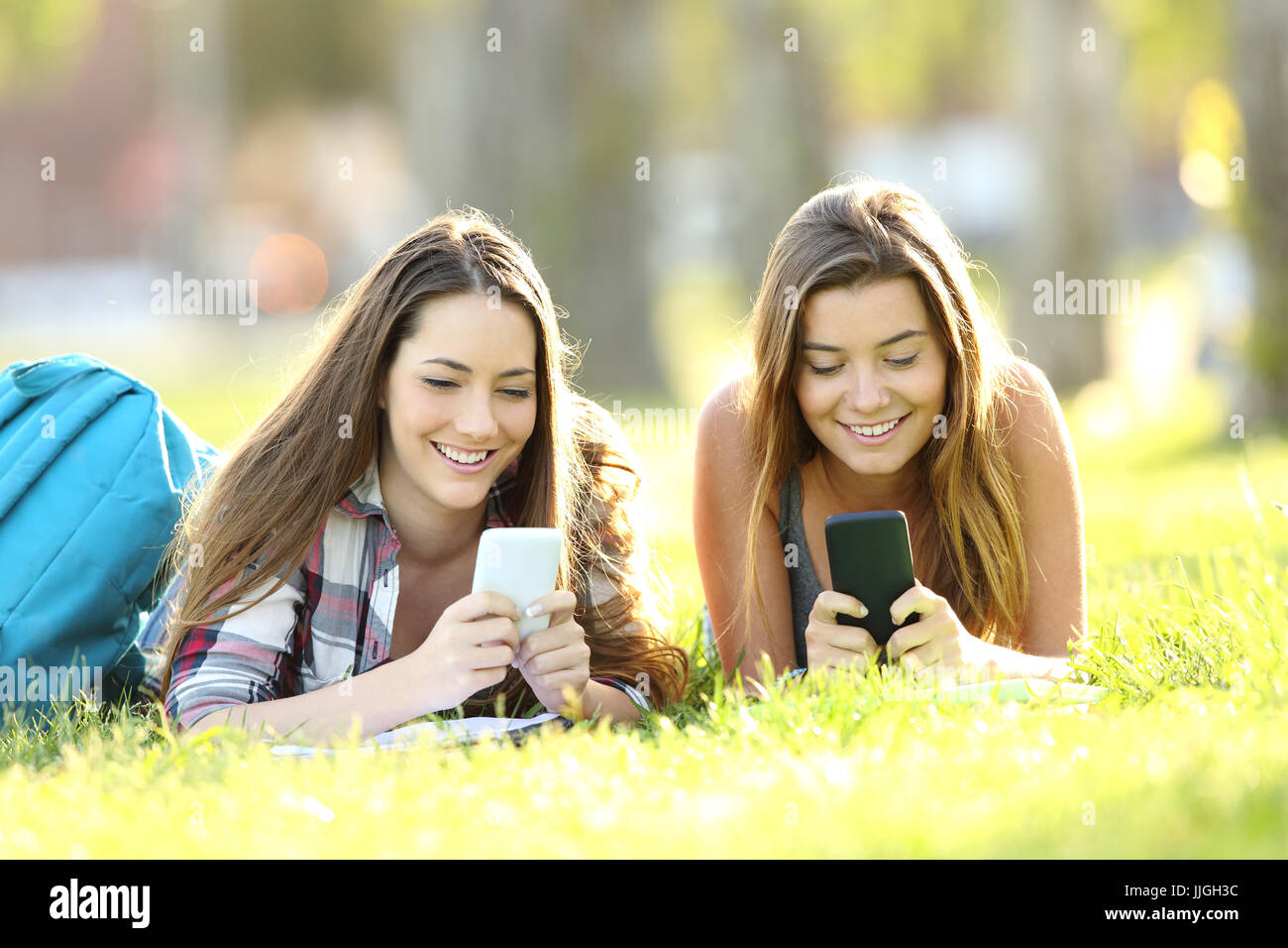 Front view of two students texting in their smart phones lying on the grass in a park Stock Photo