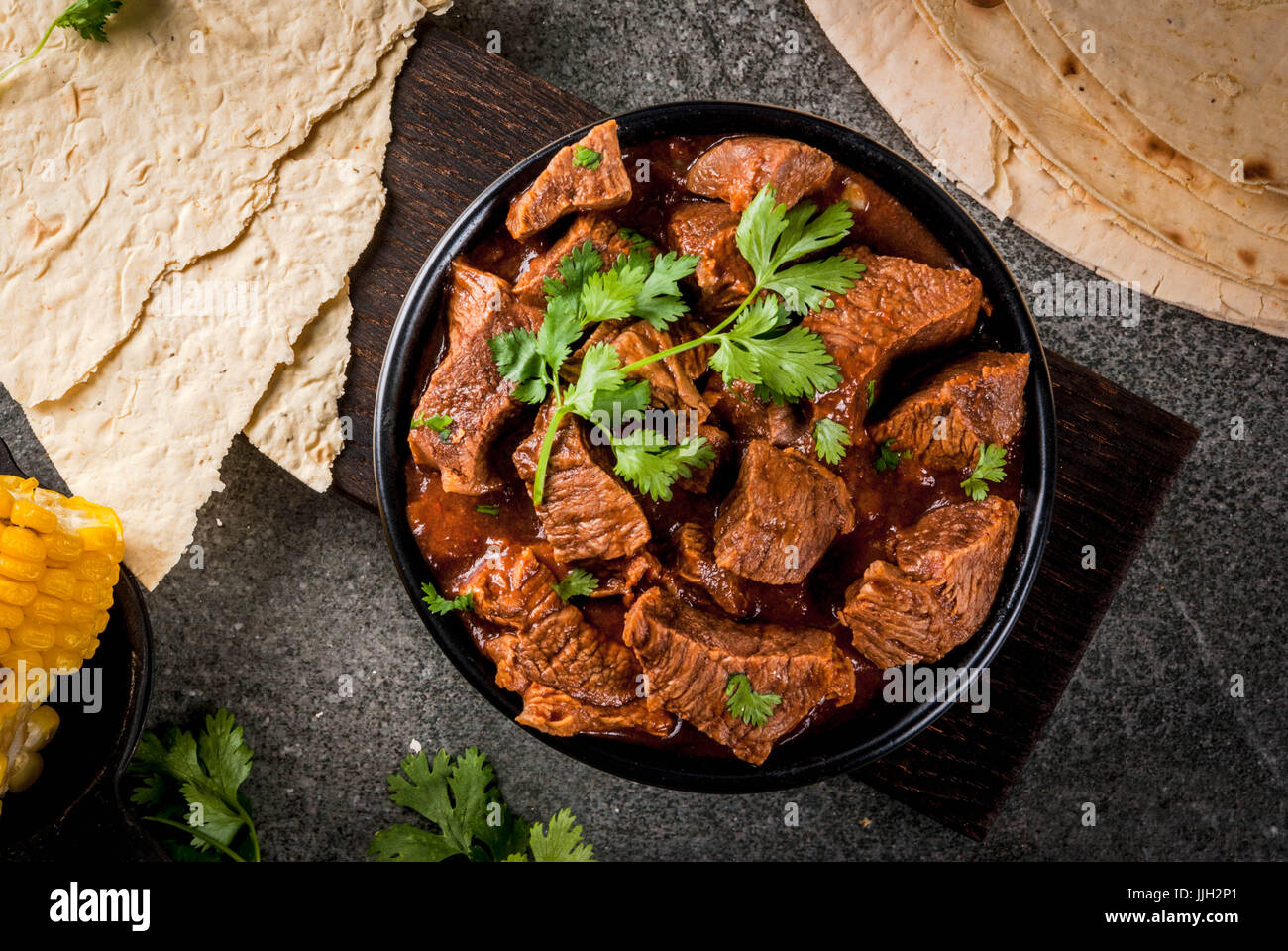 Mexican and American traditional food. Stew beef with tomatoes, spices, pepper - Chile Colorado. With tortillas.  Copy space, on black stone table Stock Photo