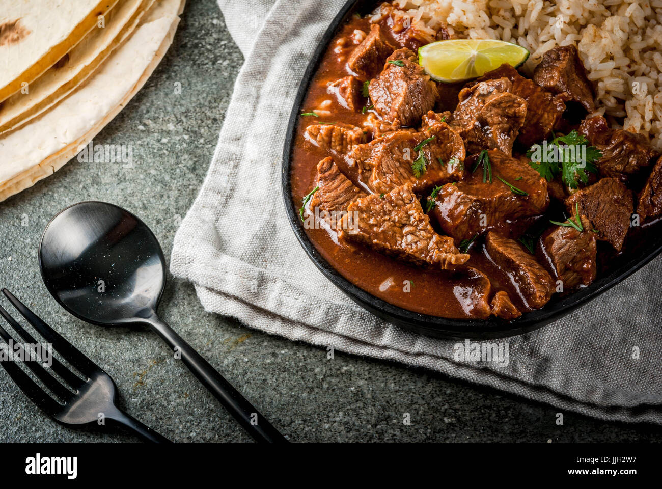 Mexican and American traditional food. Stew beef with tomatoes, spices, pepper - Chile Colorado. With boiled rice. lime, tortillas.  Copy space top vi Stock Photo
