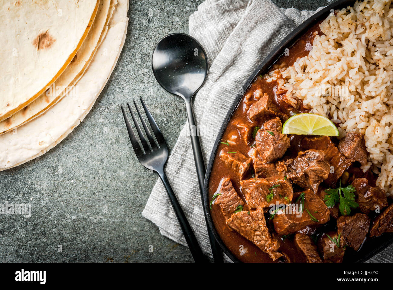 Mexican and American traditional food. Stew beef with tomatoes, spices, pepper - Chile Colorado. With boiled rice. lime, tortillas.  Copy space top vi Stock Photo
