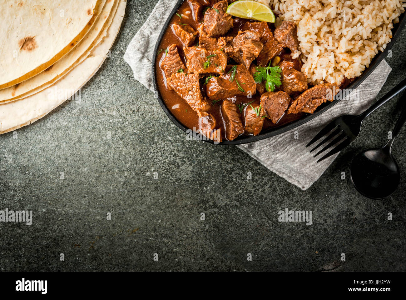 Mexican and American traditional food. Stew beef with tomatoes, spices, pepper - Chile Colorado. With boiled rice. lime, tortillas.  Copy space top vi Stock Photo