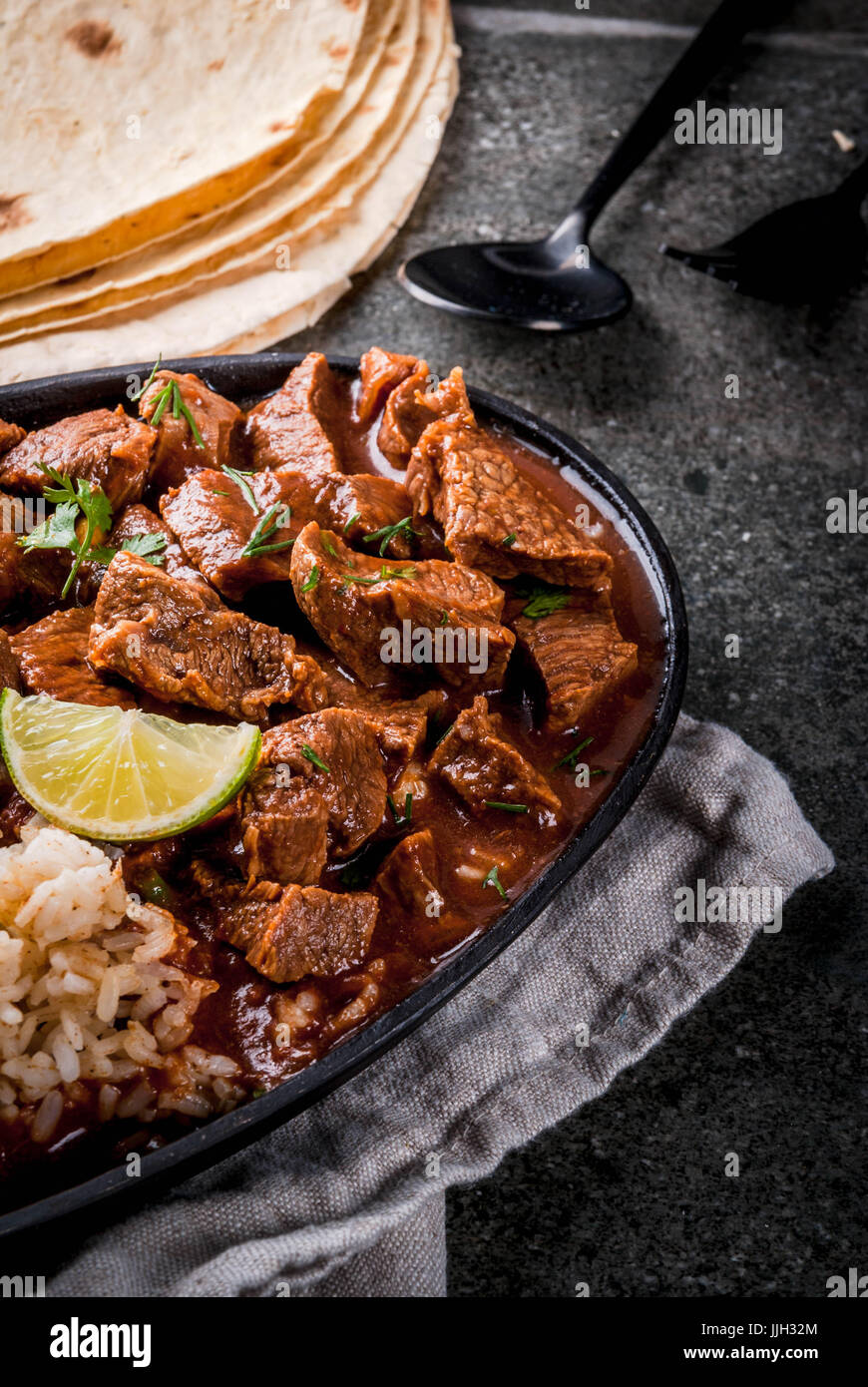 Mexican and American traditional food. Stew beef with tomatoes, spices, pepper - Chile Colorado. With boiled rice. lime, tortillas.  Copy space. On bl Stock Photo