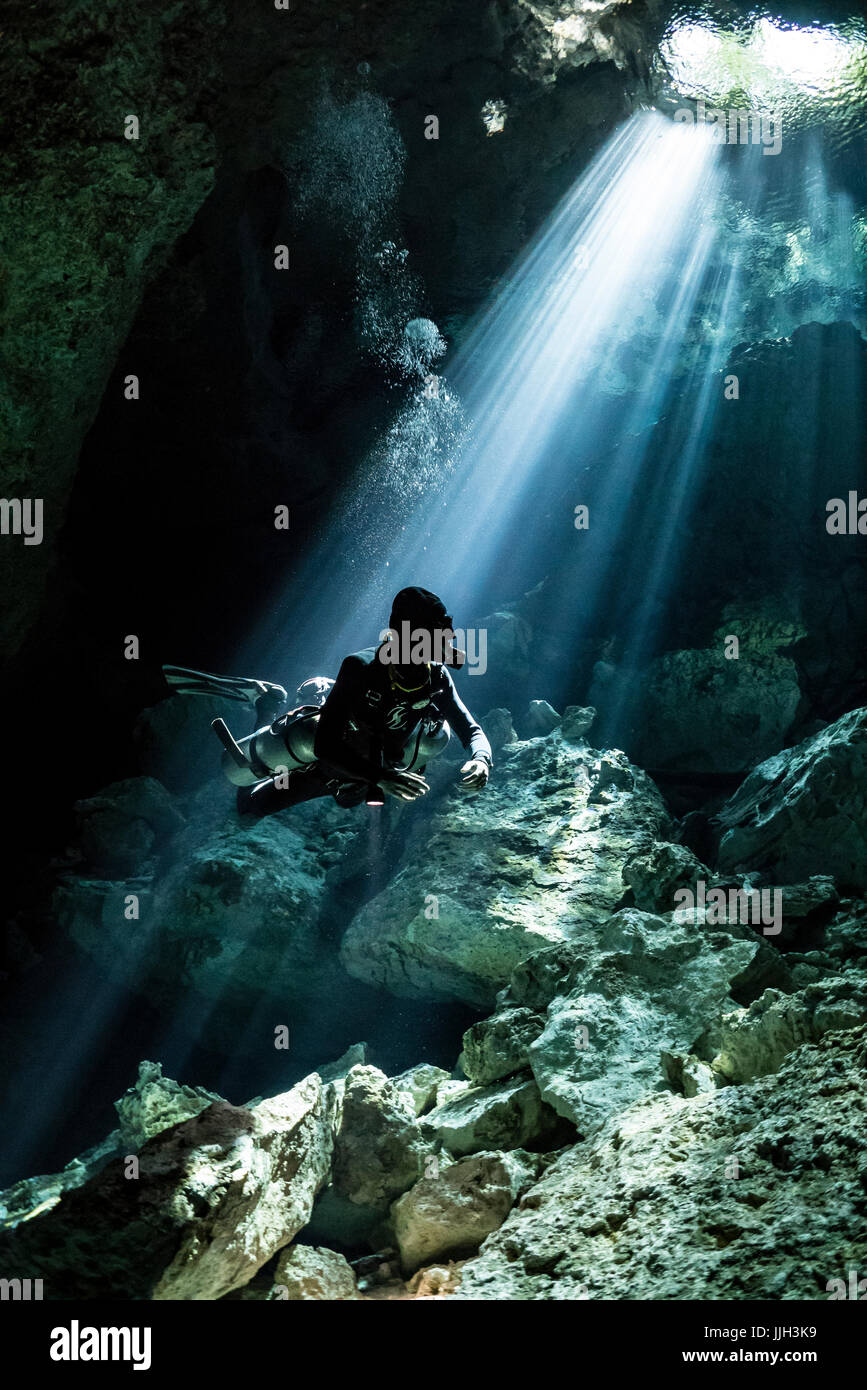 A cave diver pauses to reflect on crisp light rays  entering Mexico's Yucatan cave system. Stock Photo