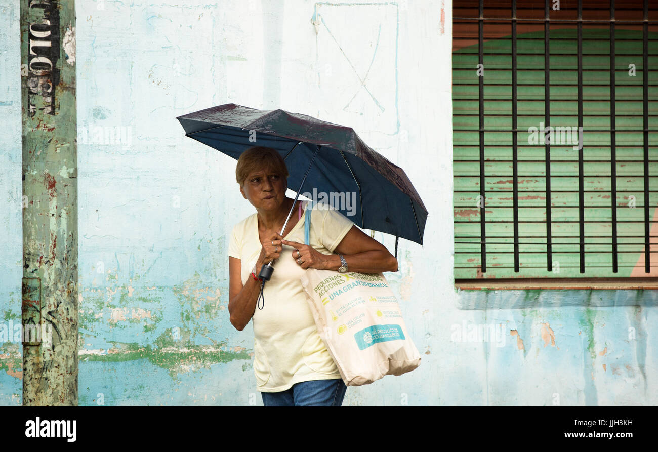 An inquisitive Argentinian woman appears concerned while walking down the street with an umbrella in the rain. Stock Photo