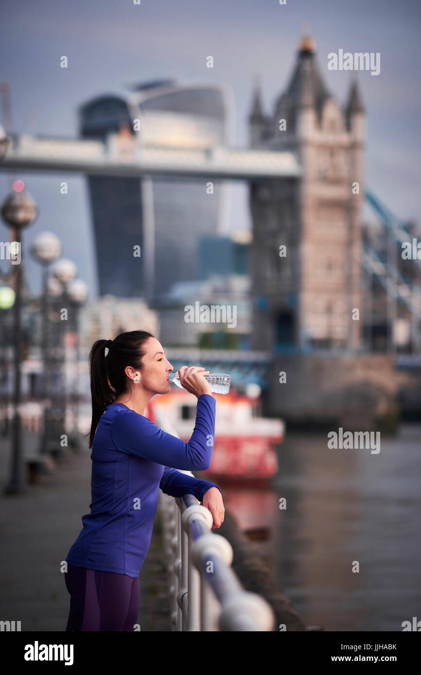 A woman resting after a run alongside the River Thames in London. Stock Photo