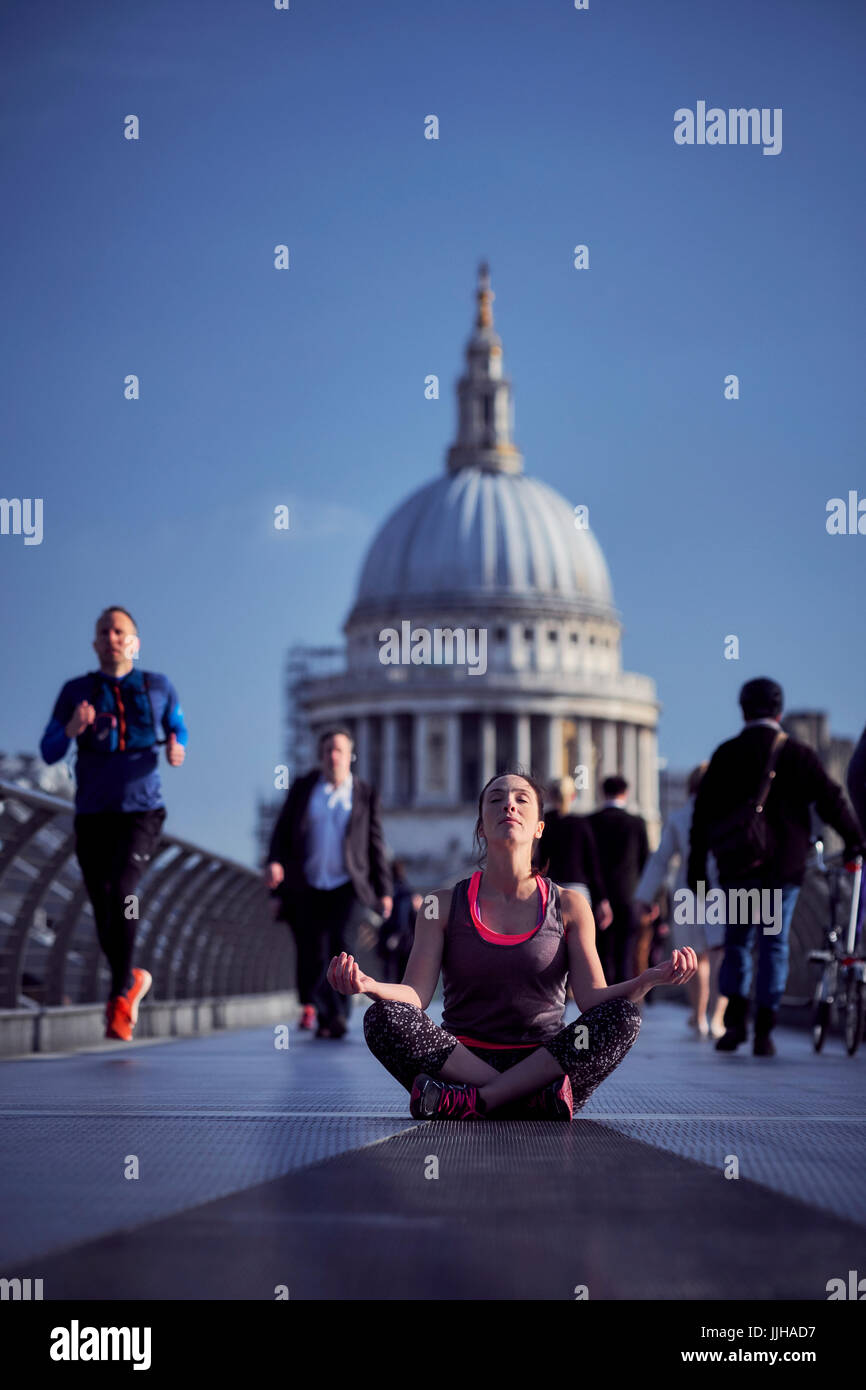 A woman meditating on the Millennium Bridge with St Paul's Cathedral in the background. Stock Photo