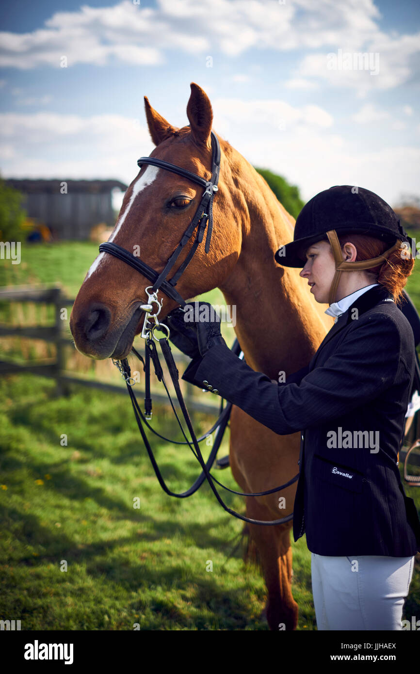 A young woman tacking up her horse prior to a ride. Stock Photo