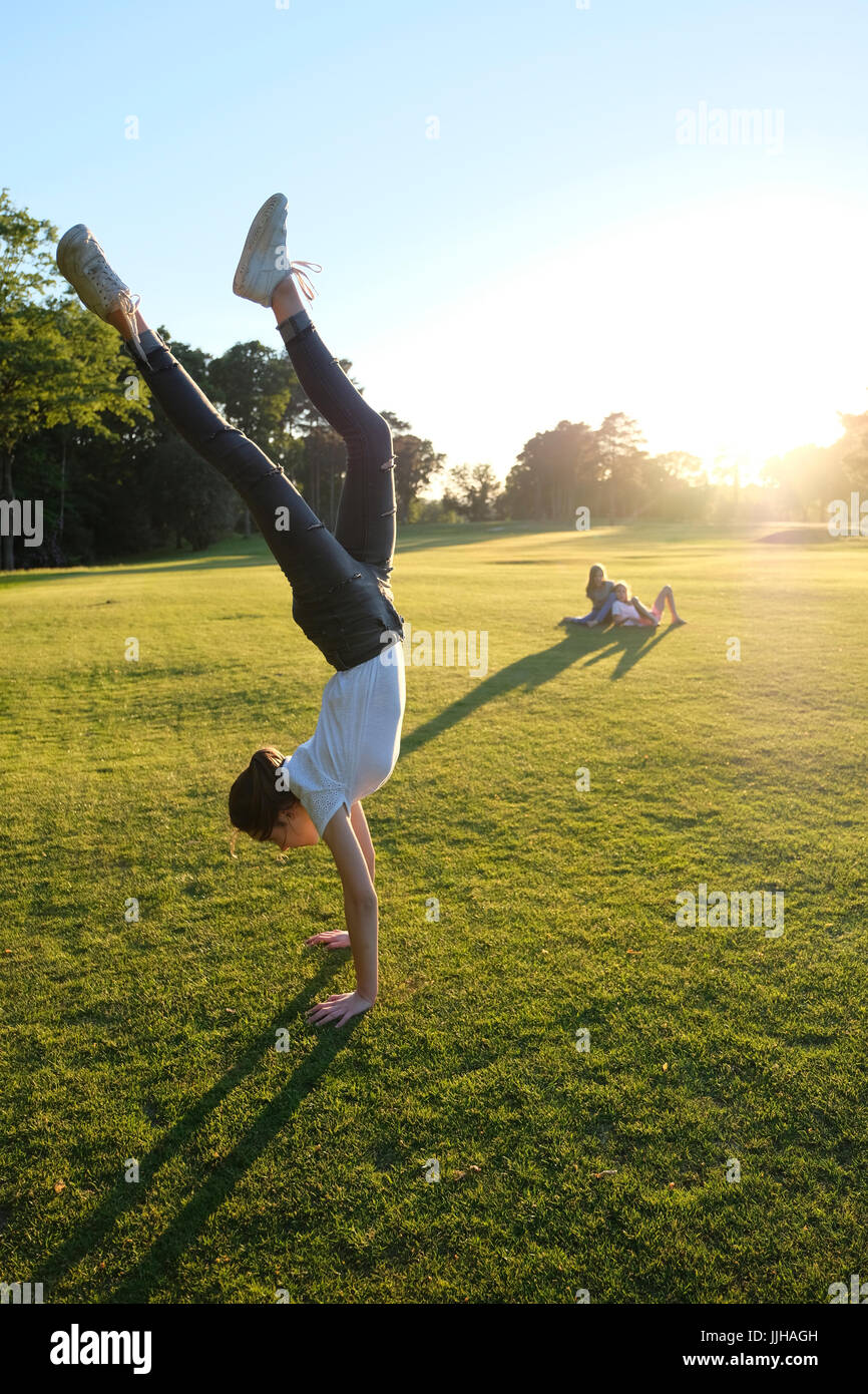 A teenage girl doing a handstand watched by her two sisters. Stock Photo