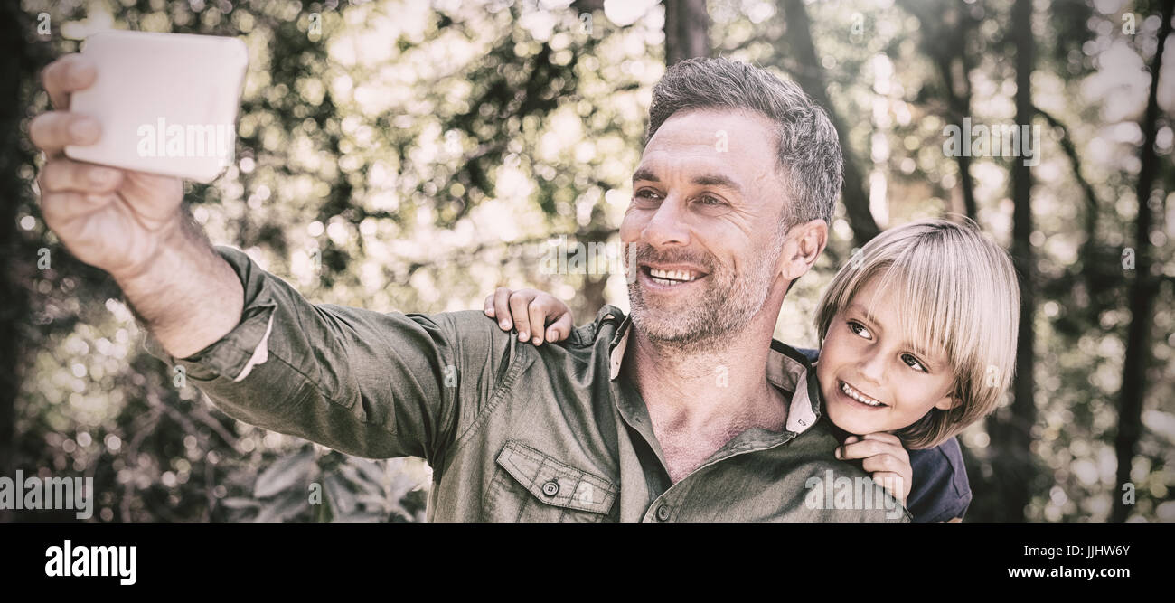 Smiling father and son taking selfie with mobile in forest Stock Photo ...