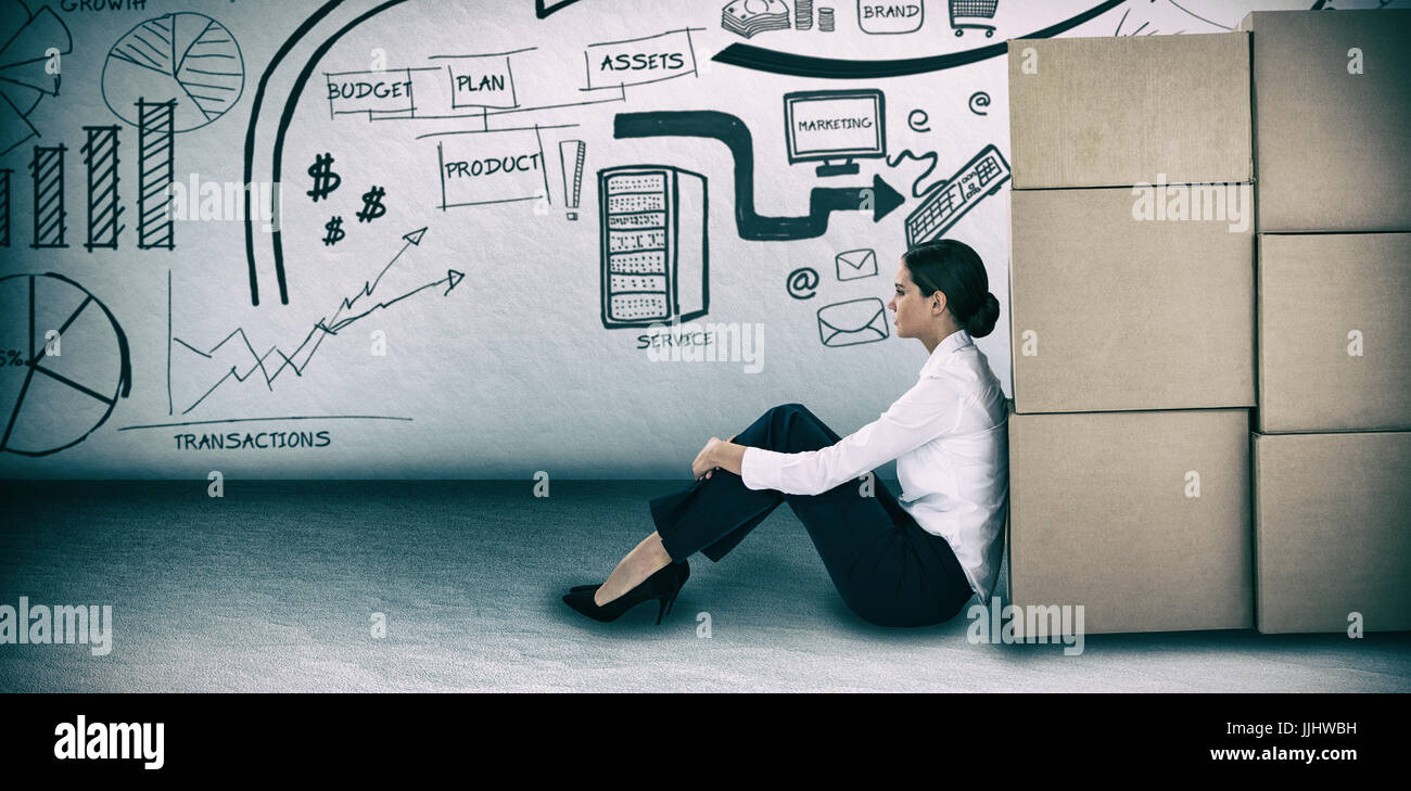 Businesswoman leaning on cardboard boxes against white background against grey room Stock Photo