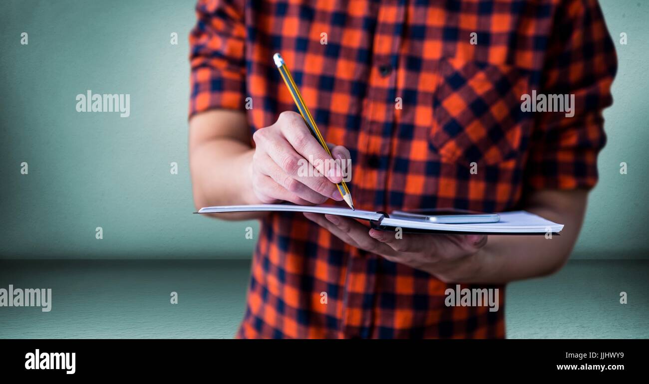 College student with mid section with notebook against green wall Stock Photo