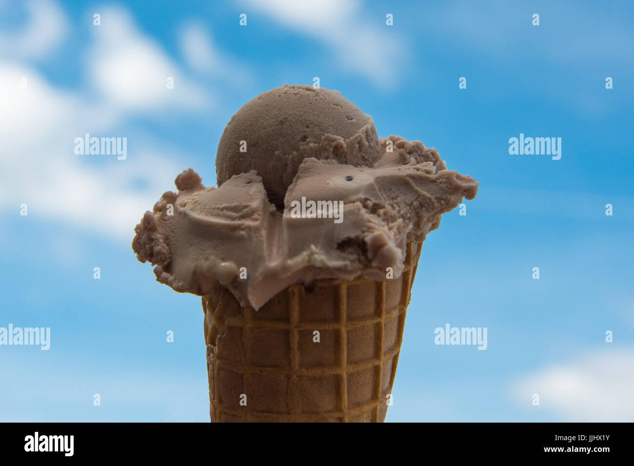 Scoop of ice in cone, close up against blue sky with clouds Stock Photo