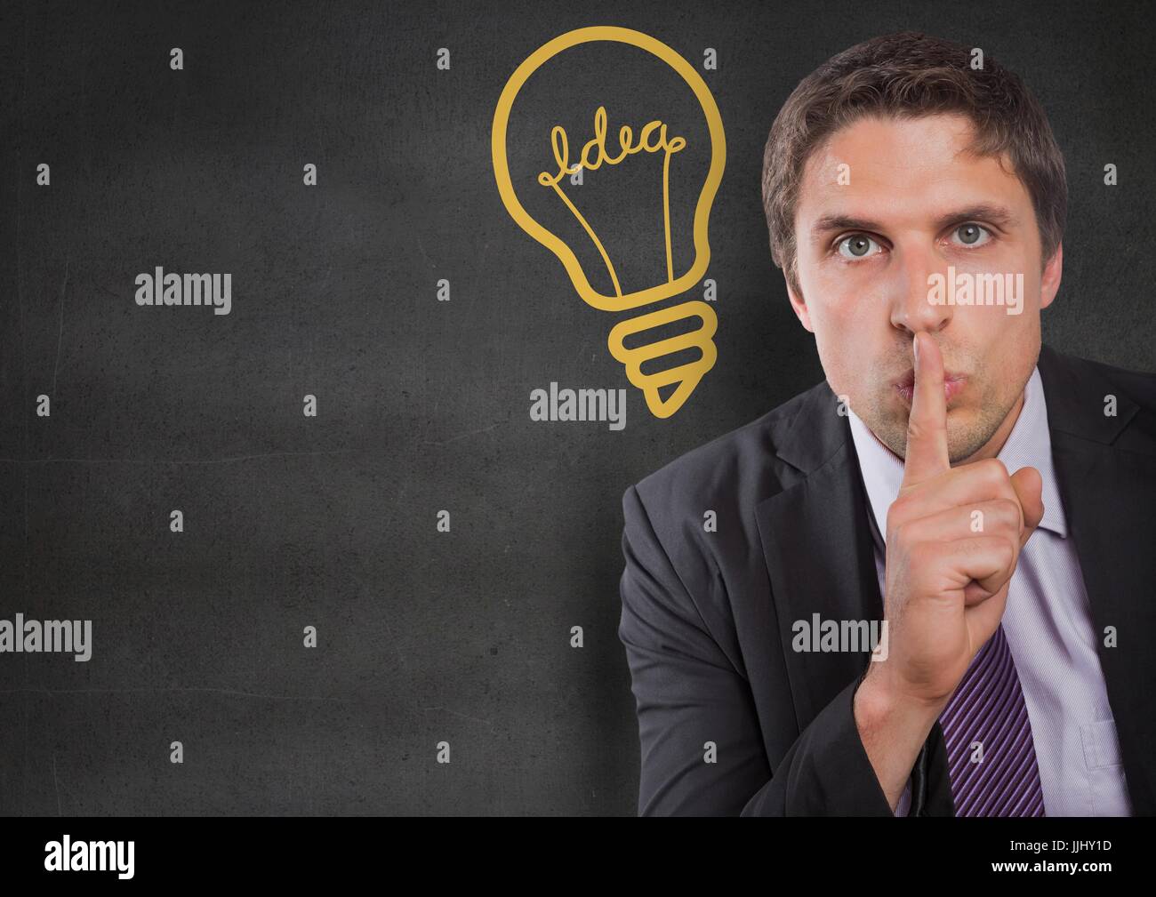 Business man finger on mouth against grey wall with yellow lightbulb graphic Stock Photo