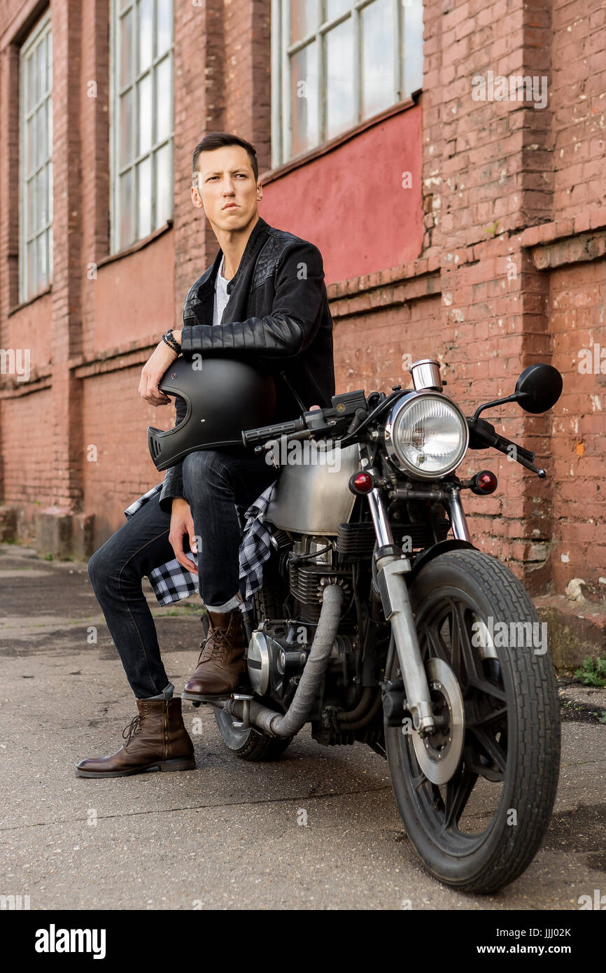 Handsome rider biker guy in black leather jacket sit on classic style cafe  racer motorcycle and hold helmet on knee. Bike custom made in vintage garag  Stock Photo - Alamy